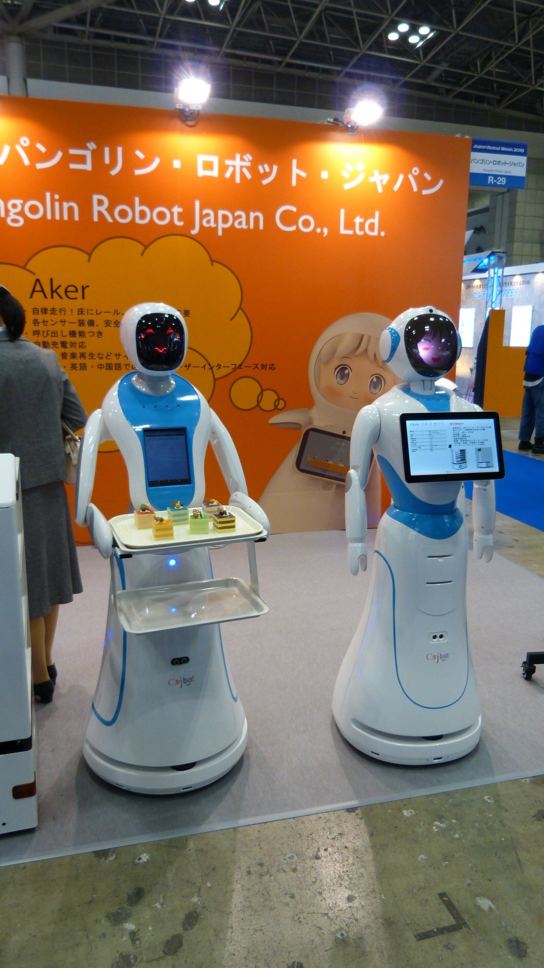 two humanoid robots with led faces.  one holds a tray of small cakes and the other has a screen on the front